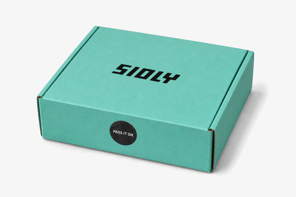 The turquoise box with SIOLY on the lid and a black “Pass it on.” sticker, pre-production visual
